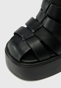 Black platform sandals with woven leather straps, a rounded open toe, and a thick sole. The texture is smooth with a matte finish.