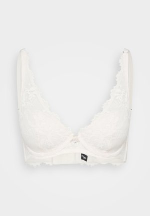 Lace bralette in off-white with triangular cups, scalloped edges, and a small metallic front clasp. Soft fabric with a textured finish.