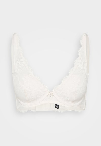 Čipkasti modrček v off-white barvi s trikotnimi skodelicami, valovitimi robovi in majhnim kovinskim sprednjim zapiranjem. Mehka tkanina z teksturiranim zaključkom.