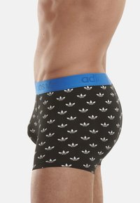 Boxer-briefs noirs avec une ceinture bleue ornée de motifs répétitifs de petits logos Adidas blancs. Fabriqués en tissu extensible et lisse.