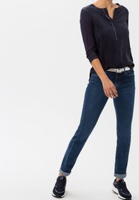 Marineblaues Langarmoberteil mit rundem Ausschnitt und einer Knopfleiste vorne, kombiniert mit eng sitzenden, dunklen Jeans und schwarzen Sneakern.