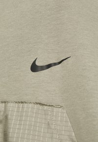 Šedá látka s hladkým povrchem má výrazné černé logo Nike a část se šachovnicovým vzorem prošitou podél spodního okraje.