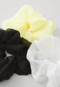 Set di tre scrunchies nei colori giallo, nero e bianco. Realizzati in tessuto trasparente con una consistenza morbida e fluida e un design arricciato.