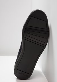 Černé tenisky s texturovanou gumovou podrážkou, s hladkým povrchem a detailem loga na patě. Navrženo pro odolnost a přilnavost.