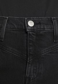 Black denim jeans featuring a silver CK logo button, visible stitching, and a classic five-pocket design.