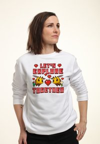 Felpa bianca con design grafico pixelato che presenta il testo "ESPLORIAMO INSIEME", api gialle, cuori ed elementi floreali.