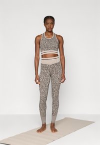 Αθλητικό σετ σε γήινες αποχρώσεις, με ένα μοτίβο crop top και ψηλόμεσα κολάν με υφασμάτινες λεπτομέρειες. Στρώμα από κάτω.