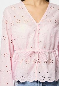 Lyserød bluse med blomsterbroderi, V-hals, lange ærmer, indsamlet talje med bånd, bølget kant og knapdetaljer. Letvægtsstof.