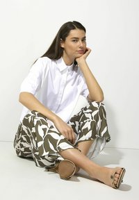 White collared shirt, short sleeves, paired with flowy olive and white patterned pants. Wearing brown open-toe sandals. Smooth texture.