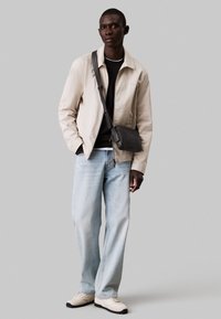 Light beige jacket, black sweater, light blue jeans, and cream sneakers. Black crossbody bag. Simple design with relaxed fit.
