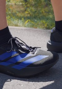 Baskets de course noires avec des rayures bleues, tige texturée et lacets noirs. Présente une semelle amortissante et un design léger.