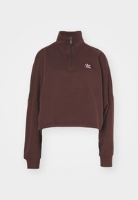 Brun kort sweatshirt med hög krage och halvdragkedja, med en liten logotyp på bröstet och långa, avslappnade ärmar.