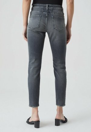 Person wearing faded grey slim-fit jeans with frayed hems and black heeled sandals, shown from the back against a plain background.