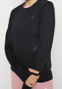 Schwarzes langärmeliges Sportoberteil aus strukturiertem Stoff, mit Rundhalsausschnitt und pinken Akzenten. Verfügt über das Adidas-Logo auf der Brust und Daumenöffnungen in den Ärmeln.