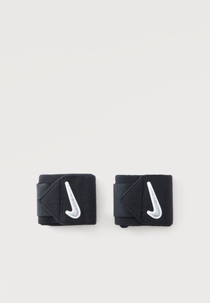 Чифт черни ленти за китки Nike с бели лога swoosh на обикновен светъл фон.