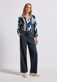 Flerfärgad mönstrad blus med blå, vit och svart rand, tillsammans med mörkgrå byxor med vida ben som har sidoränder och elastisk midja.