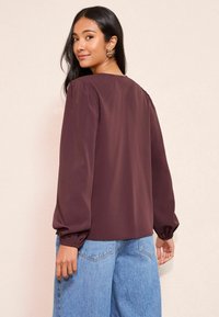 Bordo blūze ar garām pūkainām piedurknēm, gluda tekstūra un apaļa kakla izgriezums. Saskaņota ar gaiši ziliem platajiem džinsiem.