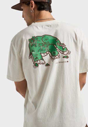 Short-sleeve beige t-shirt featuring a green elephant graphic surrounded by palm trees and rocks on the back. Soft, cotton material.