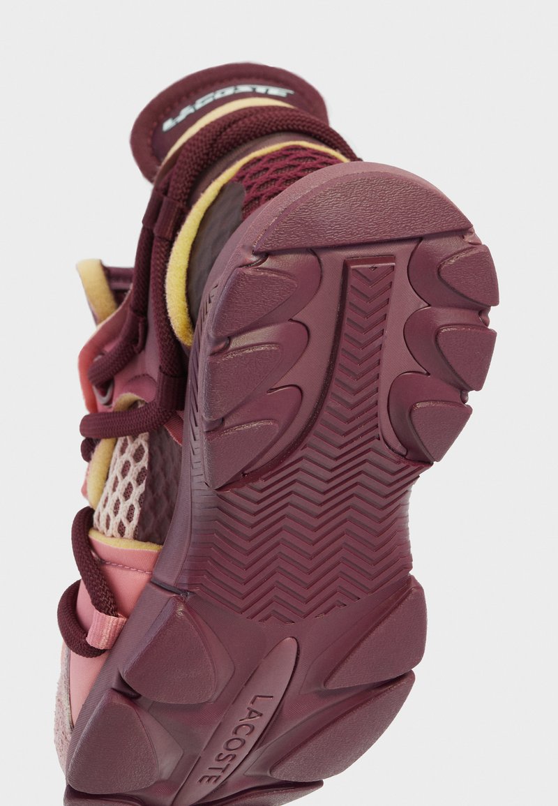 Suola di scarpa sportiva Lacoste in bordeaux e rosa, caratterizzata da gomma testurizzata con un motivo a spina di pesce e inserti in mesh sui lati.