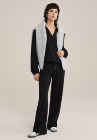 Fekete öltözet, V nyakú felsővel és bőszárú nadrággal, amit egy világosszürke, texturált, ujjatlan mellény egészít ki. A megjelenést fehér tornacipők zárják le.