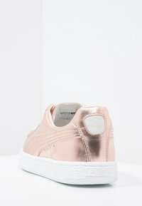 Roséguld metallisk sneaker med en slät yta, vit gummisula och en vit logopatch vid hälen. Har subtila sömnadsdetaljer.