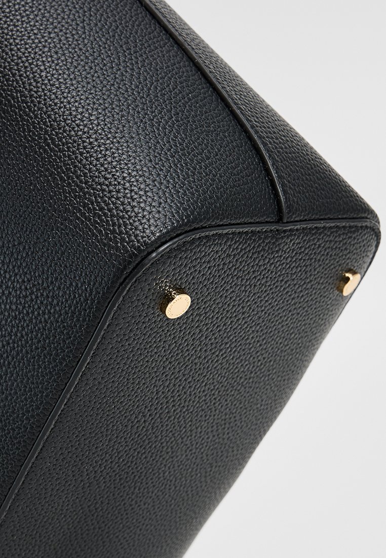 Coin de sac en cuir noir texturé avec des clous en métal doré et des détails de couture le long des bords. Forme géométrique avec des angles vifs.