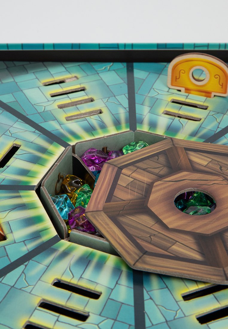 Brettspiel mit einem hexagonalen Deckel, der bunte durchscheinende Edelsteine in den Farben Grün, Lila, Blau und Gelb auf einem strukturierten Steinhintergrund zeigt.