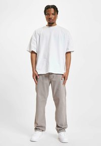 Camiseta de algodón blanca de corte oversized combinada con pantalones gris claro y zapatillas blancas. Diseño sencillo, corte relajado y colores neutros.