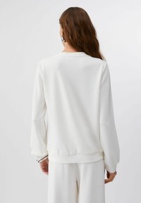 Sweatshirt blanc à col rond, manches longues et poignets côtelés. Texture douce et coupe décontractée. Présente un design lisse et sans coutures.