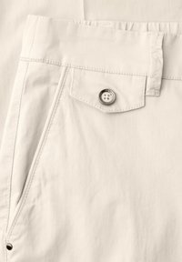 Close-up of beige pants pocket with a buttoned flap, belt loop, and stitched seams on smooth fabric.