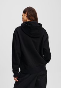 Sweat-shirt à capuche noir avec une coupe décontractée, fabriqué à partir d'un matériau doux. Équipé d'une poche kangourou et de poignets et d'un ourlet côtelés.