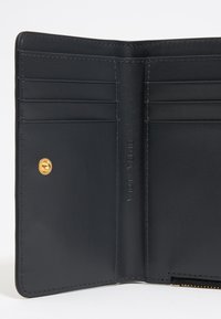 Wnętrze czarnego skórzanego portfela z wieloma niezależnymi przegródkami na karty, złotymi akcentami i wytłoczonym logo marki. Gładka tekstura i elegancki design.