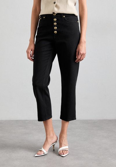 Sorte cropped jeans med høj talje, guld knaplukning og en glat denimstruktur, parret med hvide åbne hæle mules.