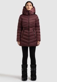 Bordo puhast plašča z visokim ovratnikom in kapuco, pasom ter žepki z zadrgo. Oblečen s črnimi legicami in zimskimi škornji do kolen.