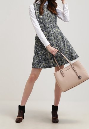 Grijs-zwart patroon a-lijn jurk met een wit overhemd met kraag eronder. Model draagt een lichtroze handtas, gecombineerd met enkellaarsjes.