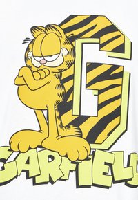 Camiseta blanca con un gato de dibujos animados amarillo y rayas negras, con los brazos cruzados, junto a una gran "G" verde y la palabra "Garfield" en letras negritas.
