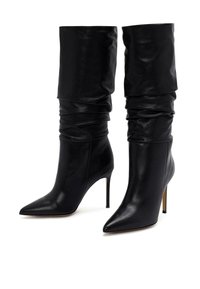 Botas de cuero negro hasta la rodilla con parte superior arrugada, punta afilada y tacón de aguja. Textura suave y diseño minimalista.