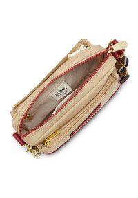 Beige Kipling crossover taske med rød lynlås, gyldent tilbehør, indvendig mærkat og stripet justerbar rem, vist åbent oppefra.