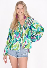 Blusa ampia e colorata con un motivo floreale in verde, rosa e blu. Presenta una chiusura con cravatta e ricami dettagliati sul colletto.