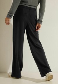 Pantalones de pierna ancha negros con una textura suave, cinturilla elástica y dos bolsillos traseros, combinados con una blusa de rayas de manga larga y zapatos blancos.