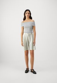 Gray off-shoulder ribbed top paired with light ivory pleated shorts and black strappy sandals, featuring relaxed fit and soft textures.