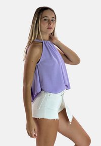 Paarse haltertop met een gedrapeerd ontwerp, gecombineerd met witte denim shorts met een rafelige zoom en een knoop aan de voorkant.