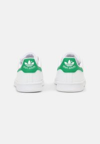 Bílé tenisky Adidas Stan Smith viděné zezadu, s zelenými patními vložkami, na kterých je logo Adidas a text "stan smith".