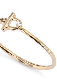 Bracelet en or avec un fermoir en forme de T ornée d'une petite pierre précieuse transparente. Surface lisse avec une texture cannelée sur un côté.