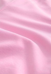 Vaaleanpunainen kangas, jossa on sileä, hieman teksturoitu pinta ja hienovarainen kiilto, esittäen pehmeitä taitoksia ja ryppyjä.