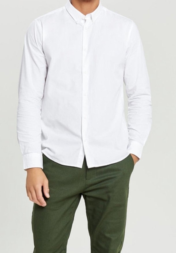 Chemise blanche à manches longues avec un col, présentant une texture lisse et une coupe ajustée, associée à un pantalon vert foncé.