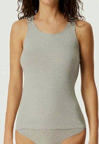 Kvinne i lys grå, ermeløs, tettsittende tanktop og matchende undertøy mot ensfarget bakgrunn.