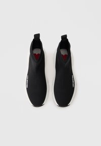 Pár čiernych teniskových ponožiek s bielymi hrubými podrážkami, text "LOVE MOSCHINO" na prednej strane a viditeľné červené srdce v každej topánke.