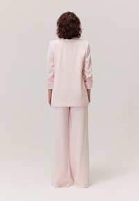 Jasnoróżowy garnitur skrojony na miarę, składający się z długiego żakietu z podwiniętymi rękawami i spodni z szerokimi nogawkami, o gładkiej teksturze i prostych, czystych liniach.