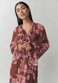 Ilga bordo spalvos suknelė su rožinėmis gėlėmis, raukiniais dekoruotu iškirpimu ir rankovėmis, bei tekstūrinėmis taškelėmis audinyje. Reguliuojama juosmens juosta.